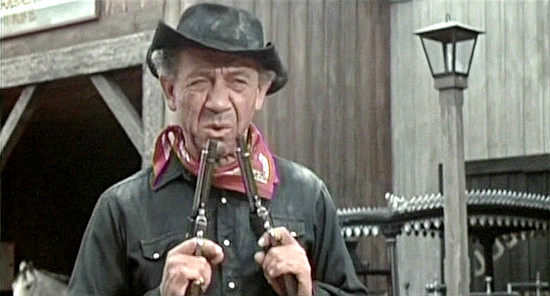 Sidney James as The Rumpo Kid, blowing smoke from his guns after leaving corpses in the street of Stodge City in Carry on Cowboy (1966)
