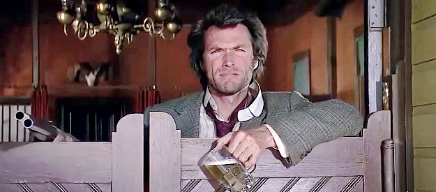 Clint Eastwood as Joe Kidd, relaxing with a beer and a shotgun as Luis Chama's men leave town in Joe Kidd (1972)