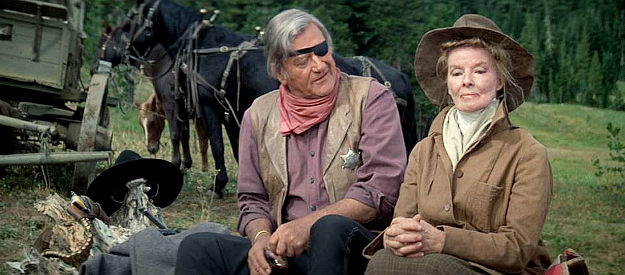 John Wayne as Rooster Cogburn and Katharine Hepburn as Eula Goodnight, trading barbs around a campfire in Rooster Cogburn (1975)