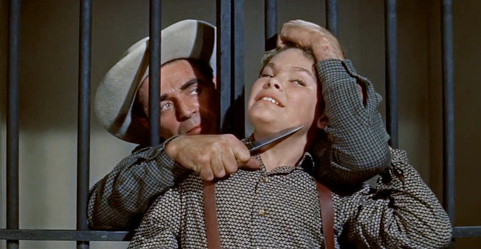 Steve Cochran as Mike Davis, holding a knife to the throad of Joel (Kim Charney) to escape jail in Quantrill's Raiders (1958)