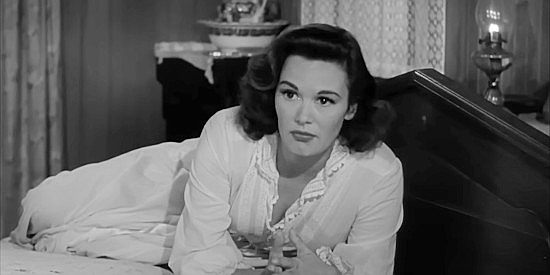 Patricia Medina as Peg Jarrett, wary of the leering stranger her husband has invited into their home in Stranger at My Door (1956)