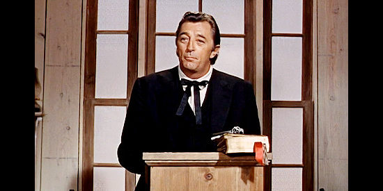 Robert Mitchum as the Rev. Jonathan Rudd, giving his first sermon in Rincon, pistol at the ready iin Five Card Stud (1968)