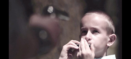 Gordon Rocks as the young boy, playing his harmonica with a pistol pointed his way in Righteous Blood (2021)
