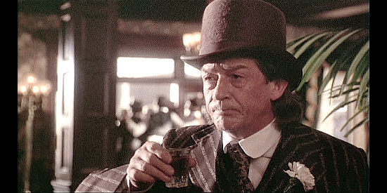 John Hurt as Charley Prince, Wild Bill's friend, enjoying a drink while he engages in a gunfight outside in Wild Bill (1995)