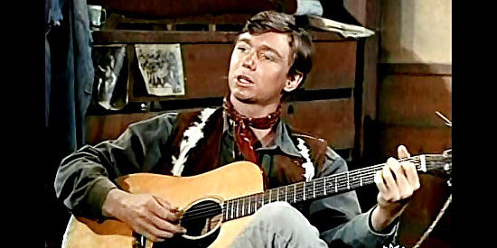 Randy Boone as Randy, a young ranch hand entertaining the bunkhouse with one of his songs in Backtrack! (1969)