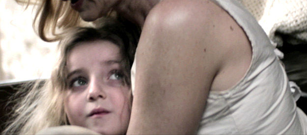 Ava Monroe Tadross as Grace, being shielded by her mother Valerie in Gunslingers (2025)