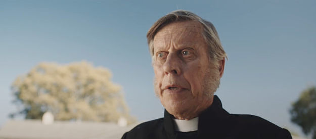 Bruce Spence as Father McGuiness, explaining the urgency of solving the murder of a leading citizen's wife and children in The Legend of Molly Johnson (2021)