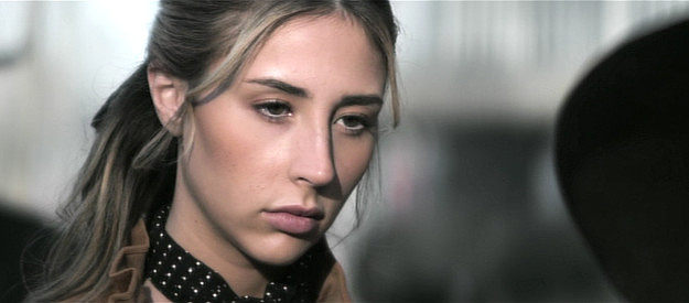 Scarlet Rose Stallone as Bella, collecting weapons from Thomas Keller in Gunslingers (2025)