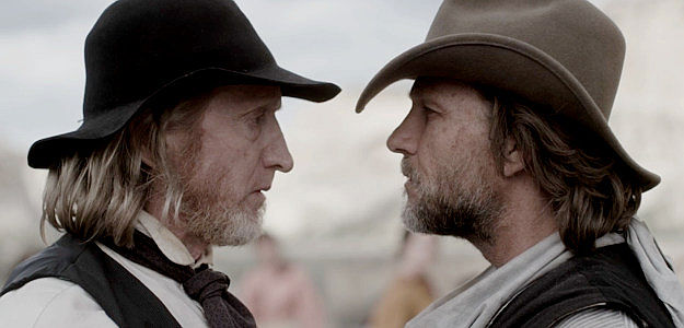 Martin Dingle Wall as Ned Campbell, trying to convince Josiah Ballard (Larry Cedar) that the bandits want more than his water and his food in This Bloody Country (2025)