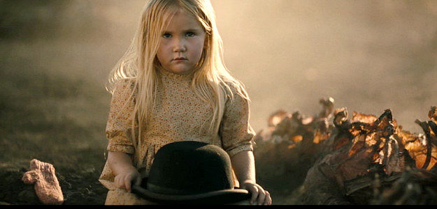 Emily Ford as the girl, gloves discarded, sitting in the middle of a burning Native American village in Killing Faith (2025)